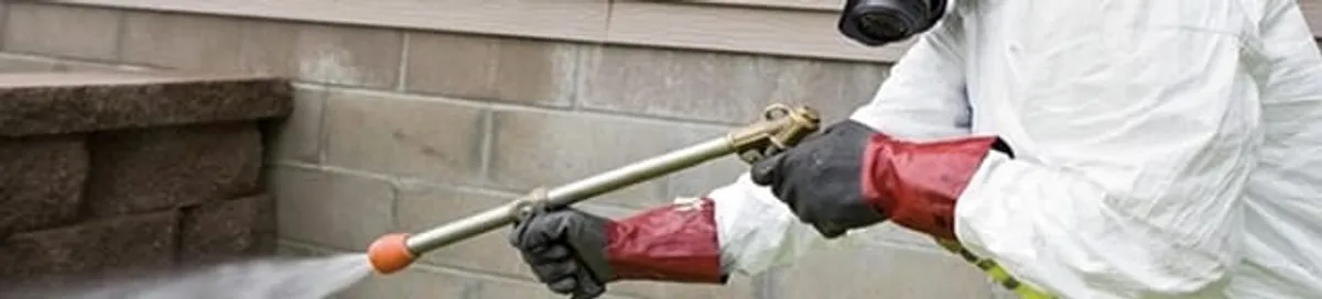 Pest control technician applying exterior insect treatment along a home foundation in Anaheim, CA
