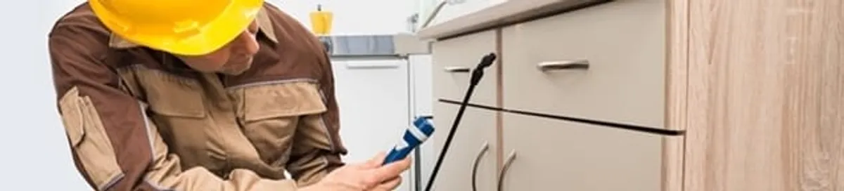 Roach exterminator applying treatment under kitchen cabinets in Anaheim, CA