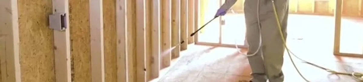 Termite treatment technician applying spray along framing and unfinished walls in Anaheim, CA